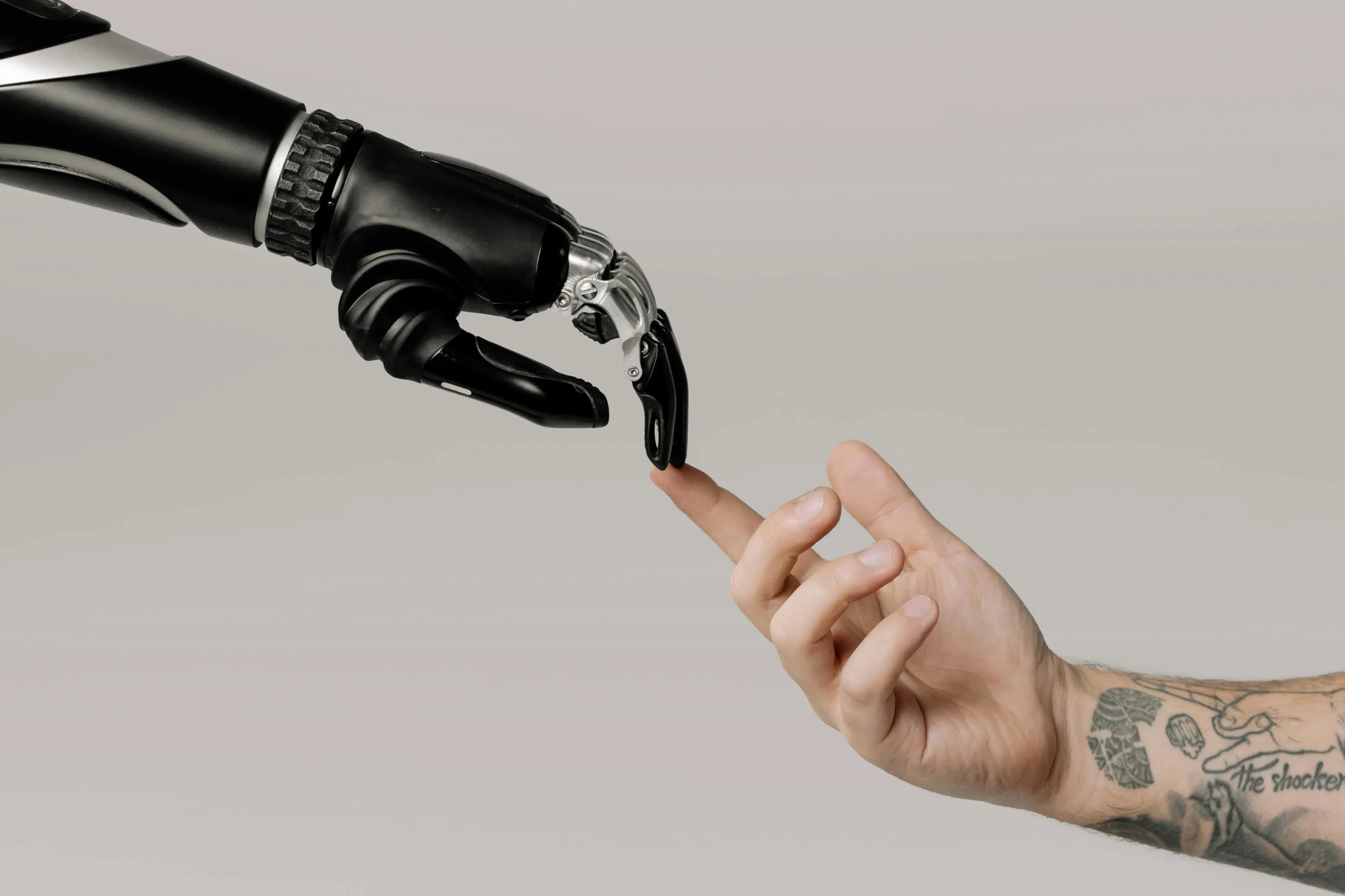 Black robotic hand reaching toward a human fingertip against a neutral background